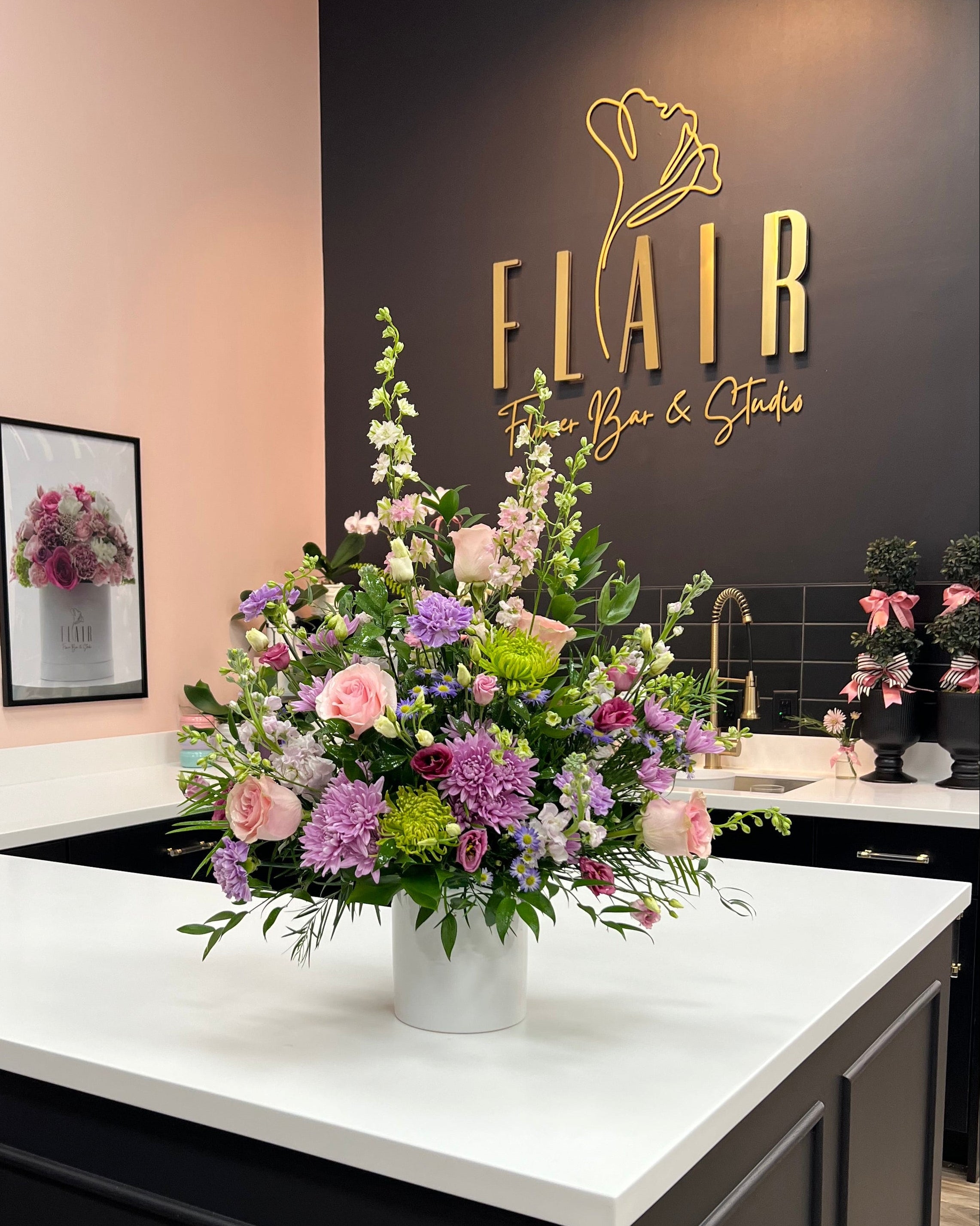 Floral arrangement on a counter with 'FLAIR' sign in the background-Florence, Kentucky Flower Shop- Cincinnati Flower Delivery