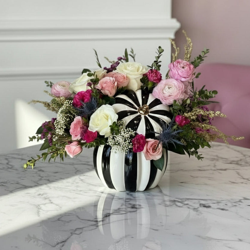 Floral arrangement in a black and white striped vase on a marble surface.