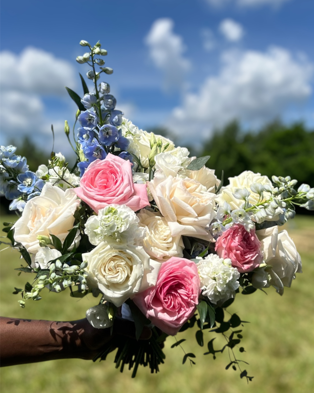 Bouquet of pink, white, and blue flowers held against a blue sky with clouds.