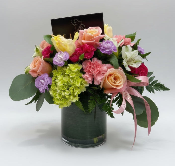 Colorful bouquet of flowers in a vase with a pink gift bag in the background.