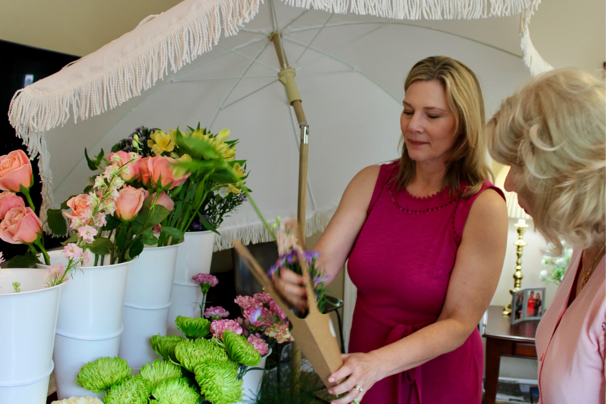 Woman in a pink dress holding a box under an umbrella with floral arrangements in the background.
