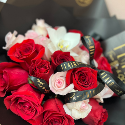 Bouquet of red and pink roses with 'Flair' ribbons wrapped in black paper