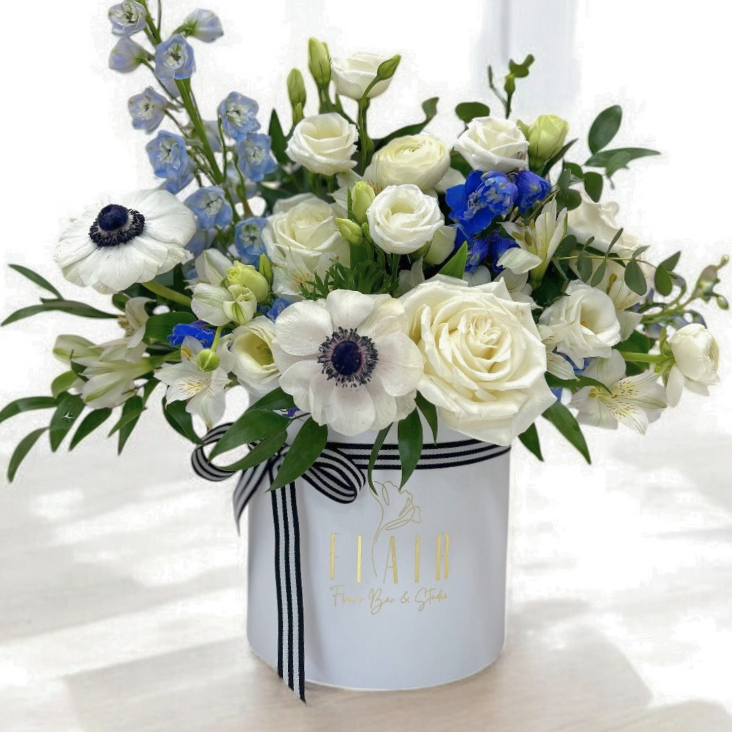 Floral arrangement in a white box with blue and white flowers on a light background