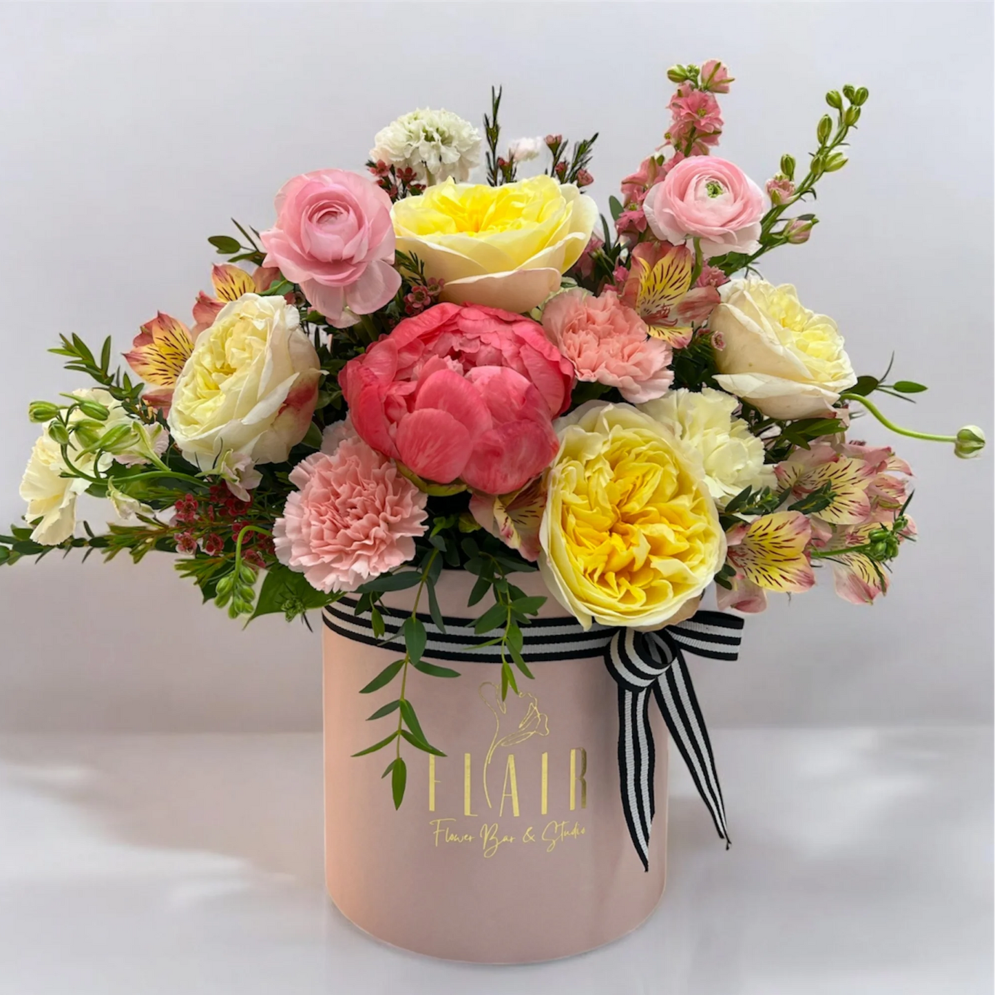 Bouquet of colorful flowers in a pink box with a brand name on a light gray background