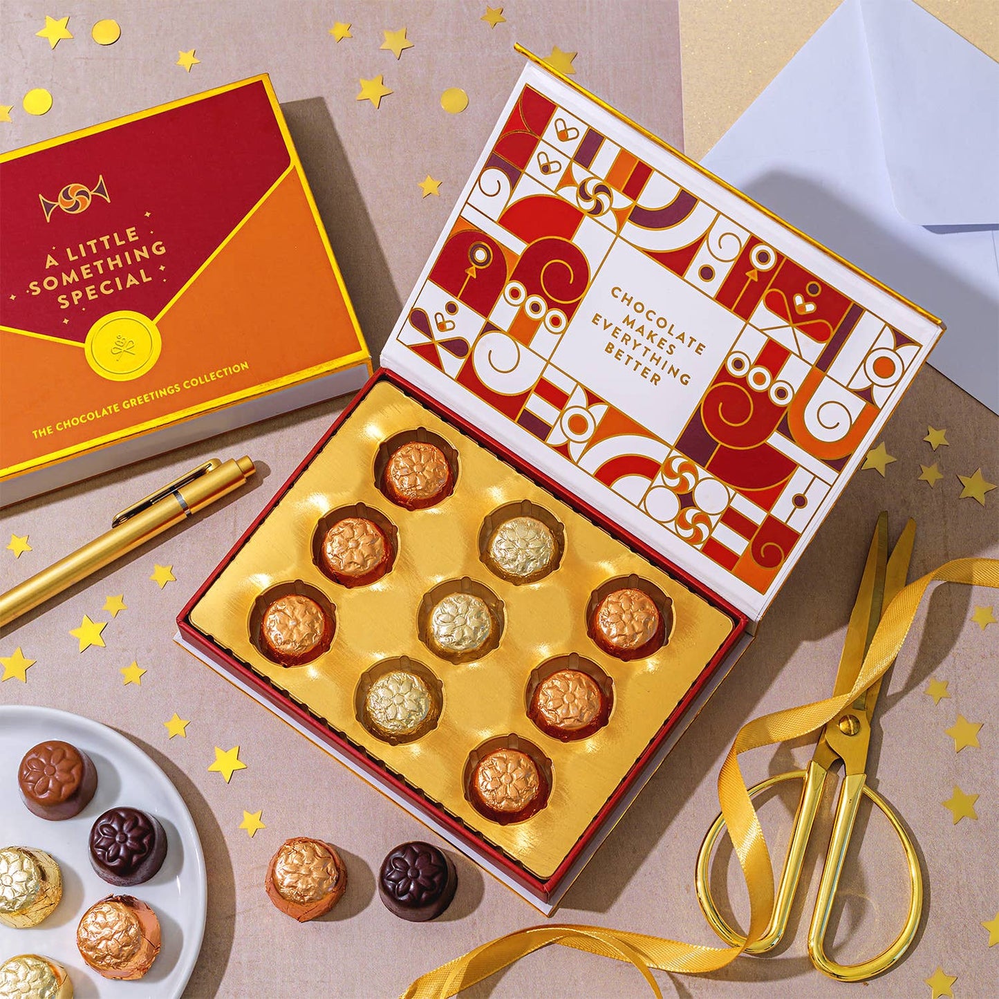 Box of chocolates with decorative packaging on a table with gold ribbon and scissors.
