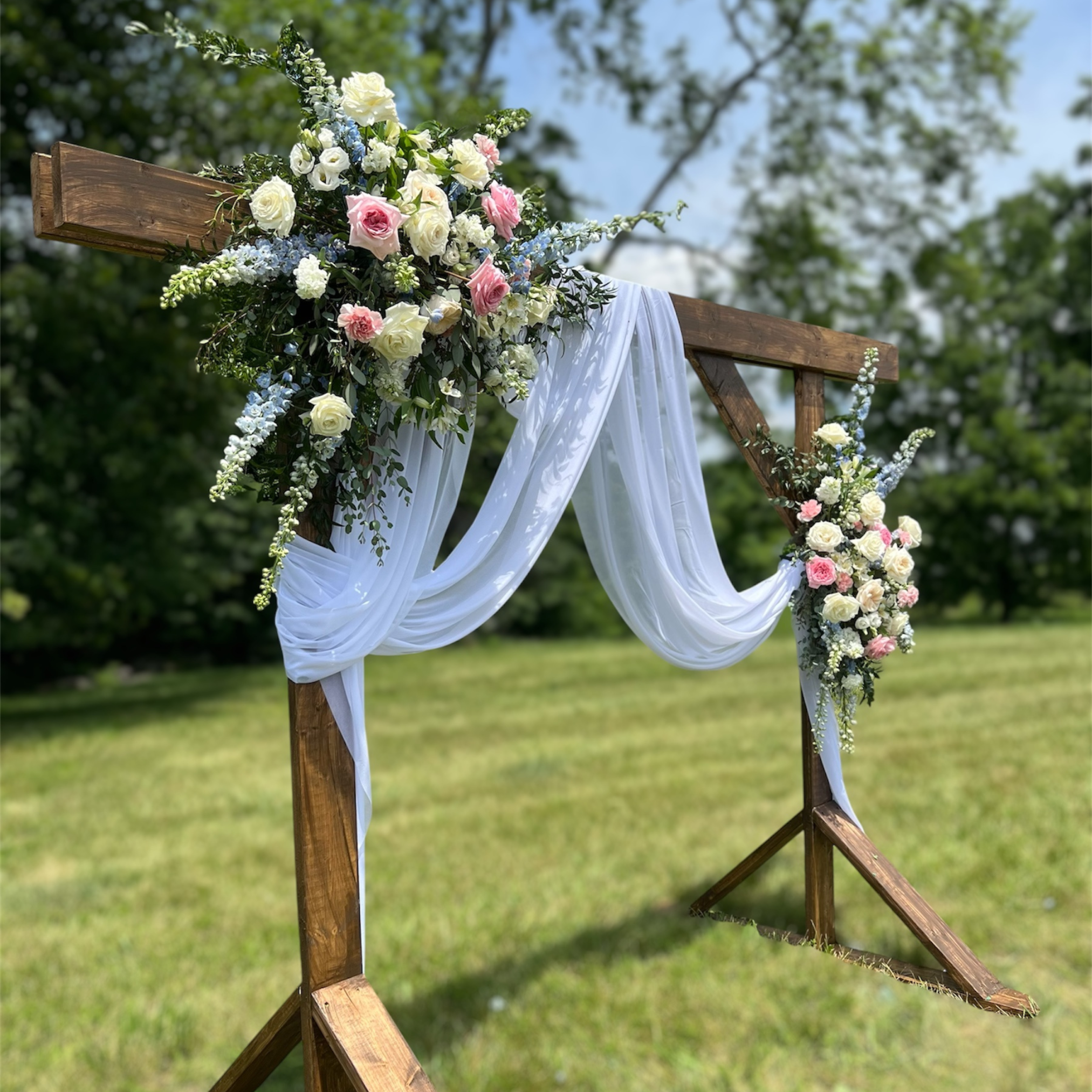 Wedding wooden arch with floral arrangements and white fabric in an outdoor setting.