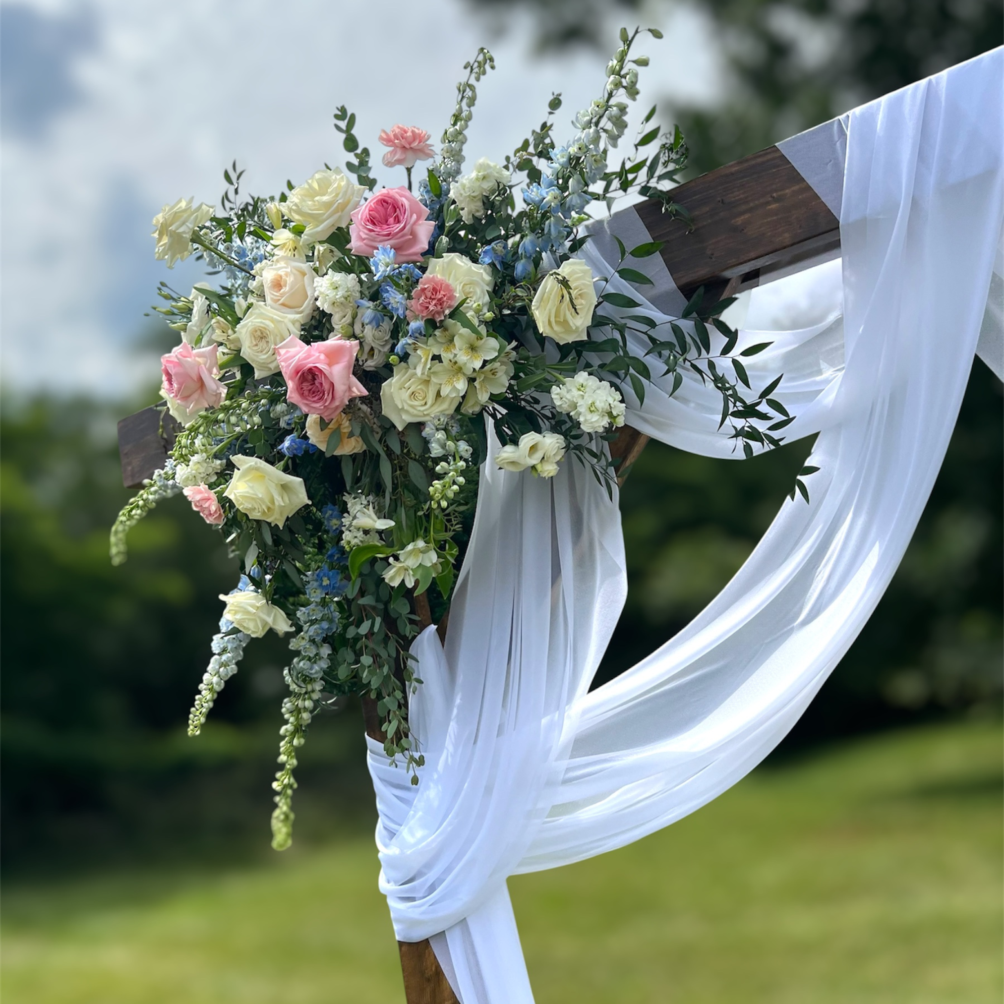 Floral arrangement on a wooden archway with greenery in the background