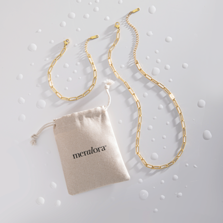 Gold chain necklace with a 'meralora' branded pouch on a textured gray background