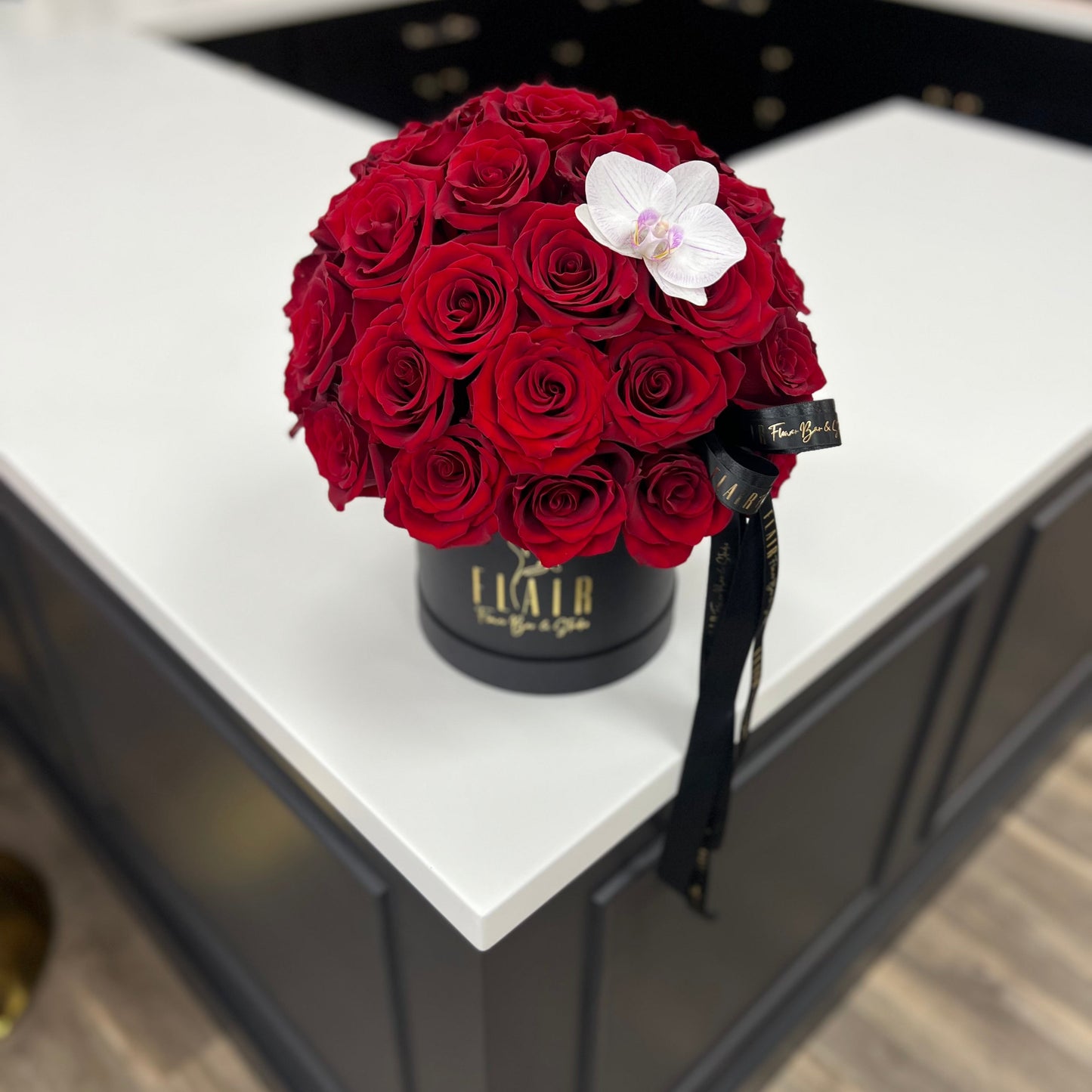 Bouquet of red roses with a white orchid in a black container on a white surface.