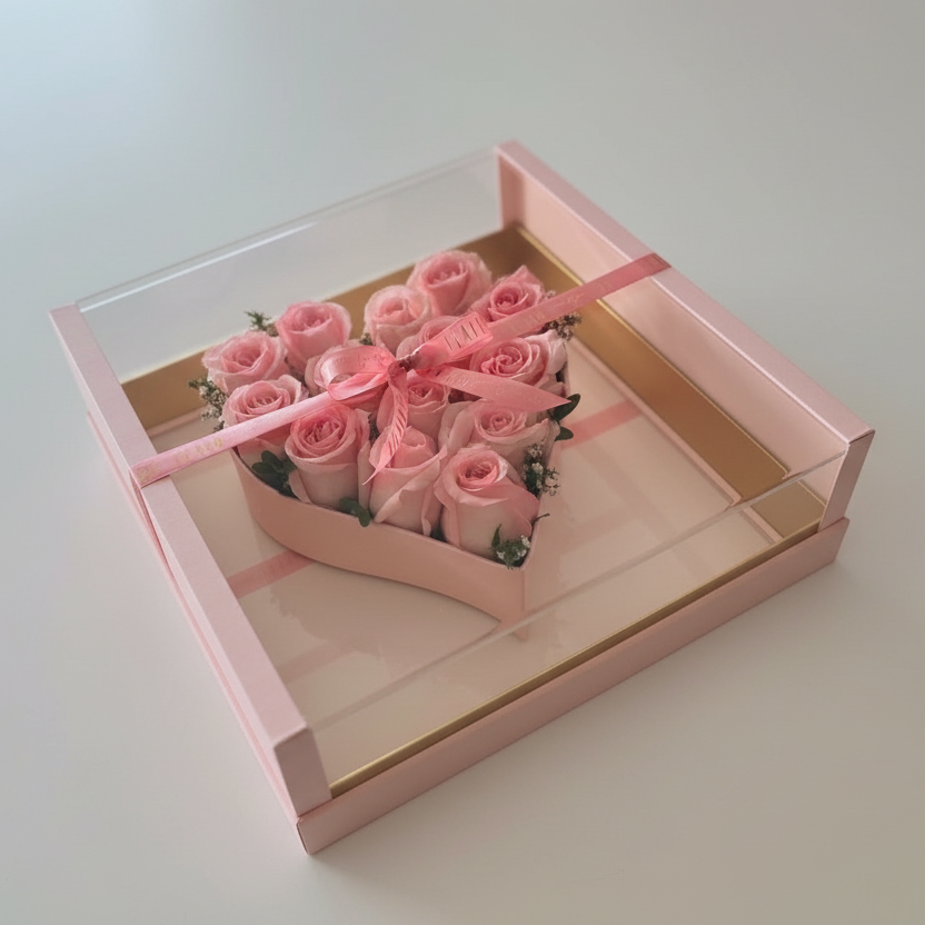 Pink roses in a decorative box with a pink ribbon on a gray surface.