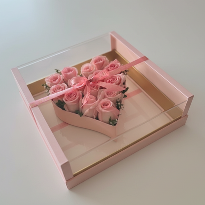 Pink roses in a decorative box with a pink ribbon on a gray surface.