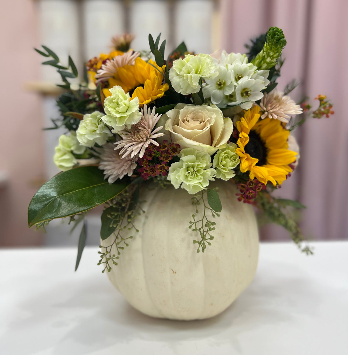 Floral arrangement in a white pumpkin on a white surface with a blurred background