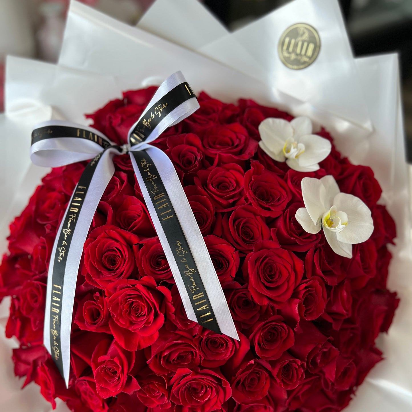 Round-shaped bouquet of red roses with a white ribbon and orchids on a white background