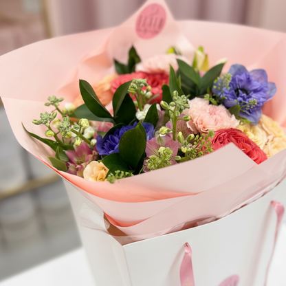 Bouquet of flowers wrapped in pink paper with a white box on a blurred background