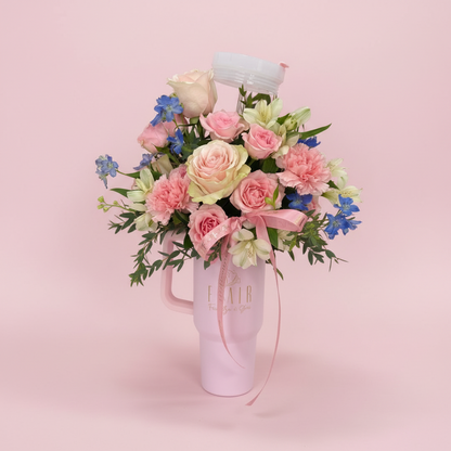 Bouquet of pink and white flowers in a pink mug on a white surface.