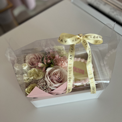 Clear box with pink roses and a yellow ribbon on a white surface