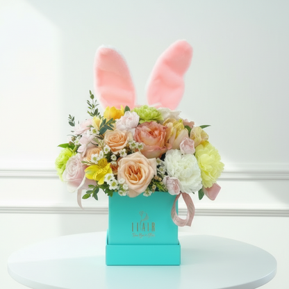 Easter floral arrangement with bunny ears on a light blue box against a beige background