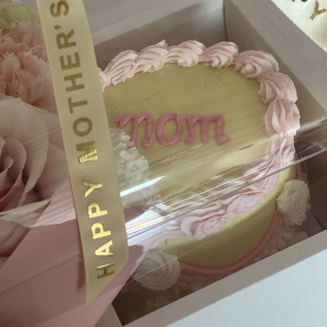 Round-shaped cake with 'mom' and 'Happy Mother's Day' text ribbon, surrounded by flowers-Flair Flower Bar