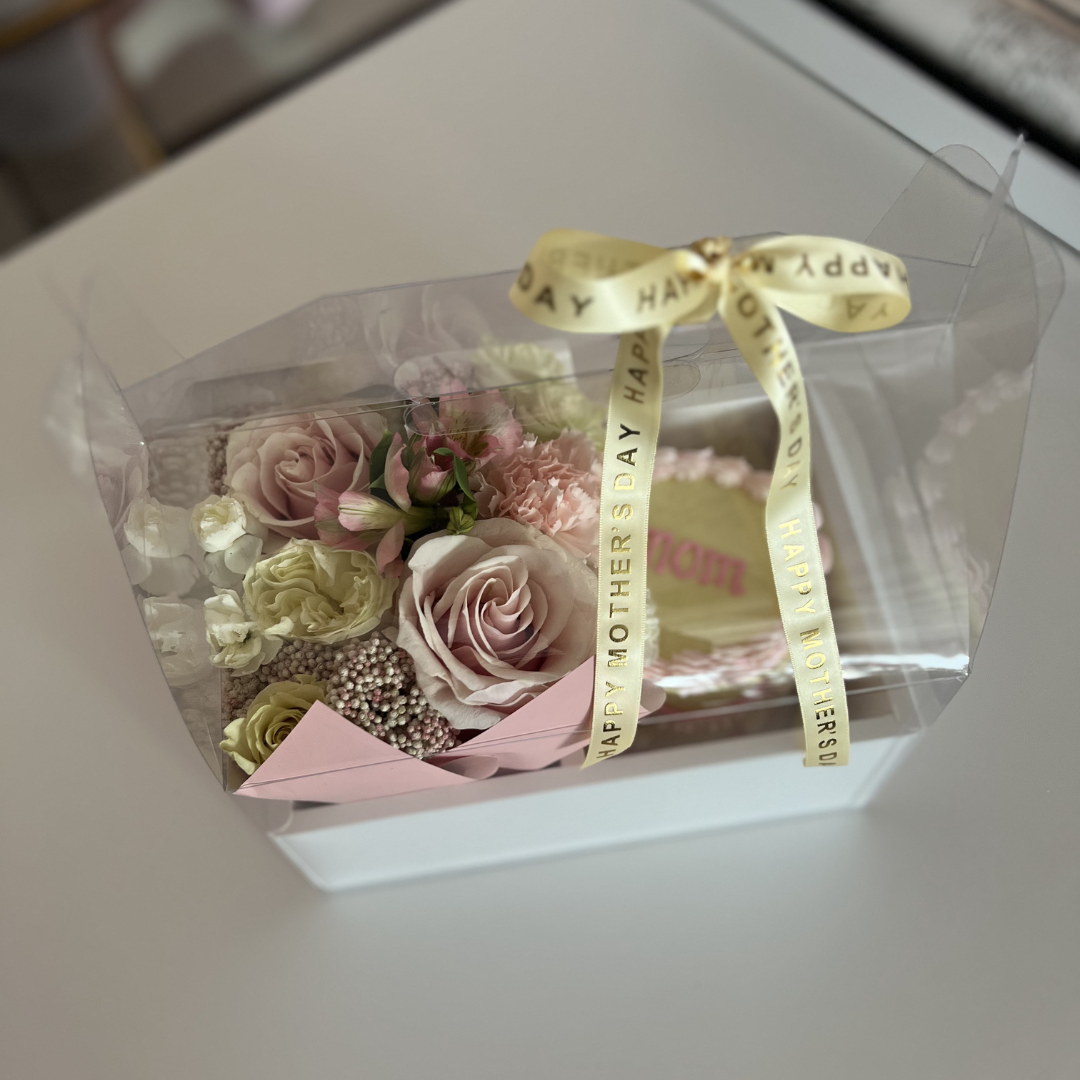 Clear box with pink roses and a yellow ribbon on a white surface