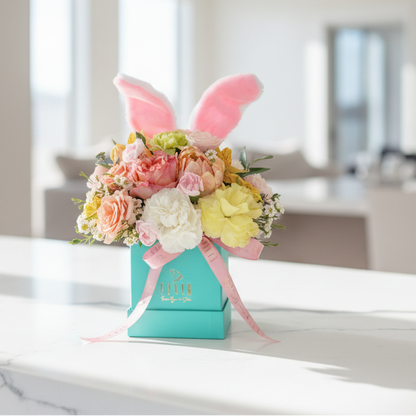 Easter floral arrangement with bunny ears in a turquoise box on a marble surface.