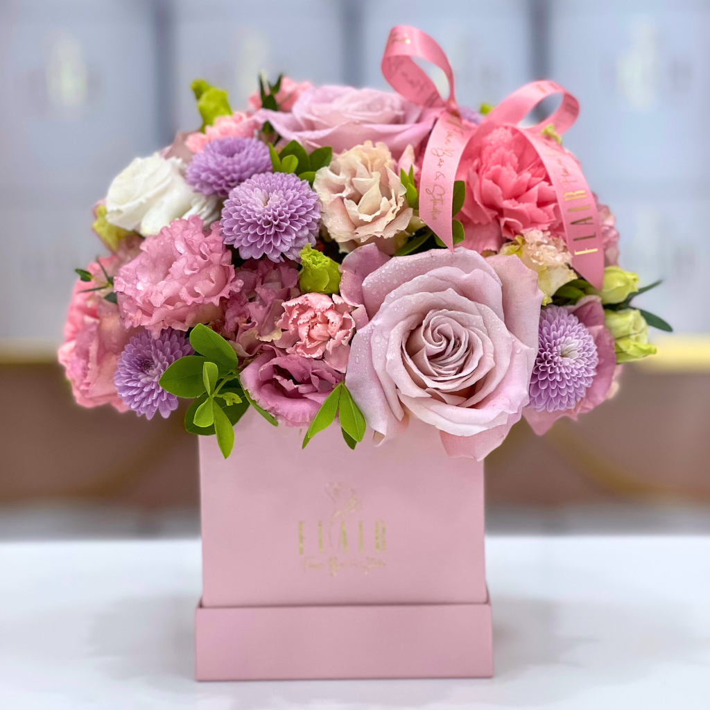 Pink floral arrangement with ribbons in a pink box on a blurred background