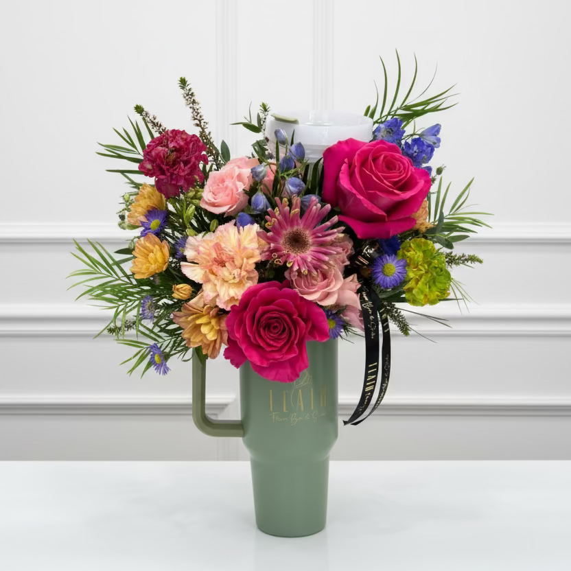 Bouquet of colorful flowers in a green vase on a white surface with a blurred background.