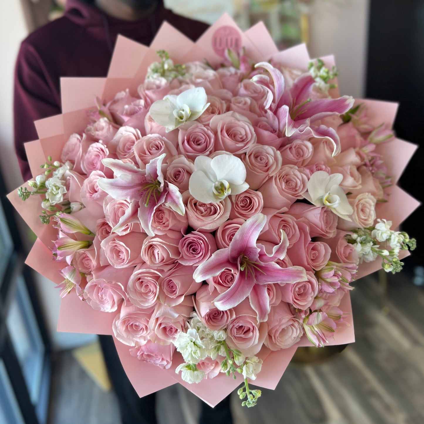 Ramo Buchon Rose Bouquet of pink roses with white accents held by a person indoors.