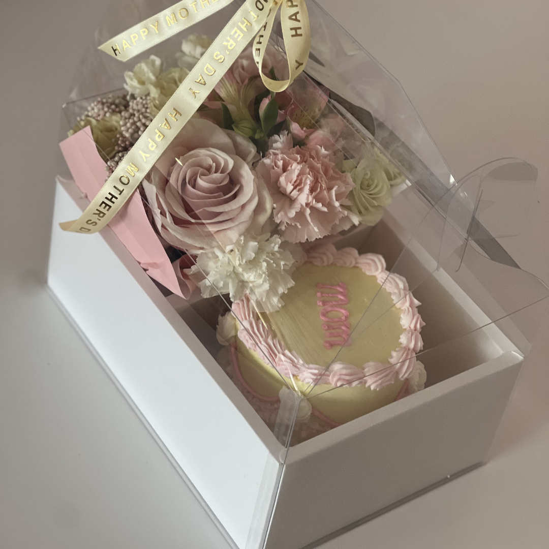 Gift set with flowers and a cake in a clear box on a white surface