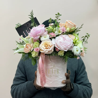 Person holding a bouquet of flowers and a box with Flair on it against a light-colored wall fretting read to go out on delivery to Cincinnati