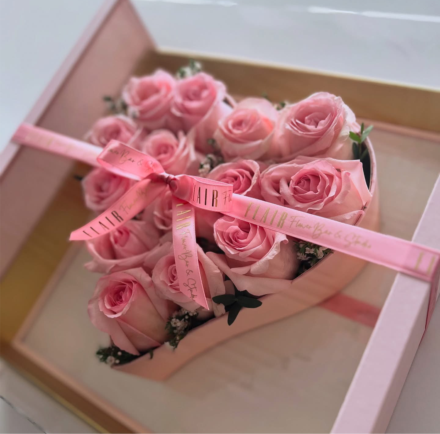 Heart-shaped arrangement of pink roses with a pink ribbon in a box.
