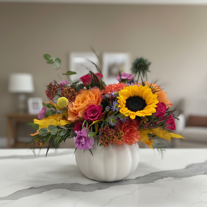 Colorful flower arrangement in a white vase on a table with a blurred indoor background
