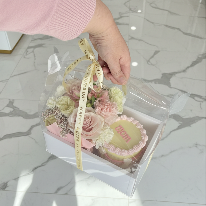Hand holding a transparent box with a bouquet of flowers and a ribbon