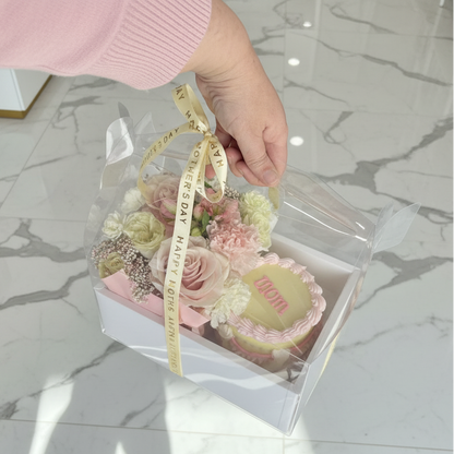 Hand holding a transparent box with a bouquet of flowers and a ribbon