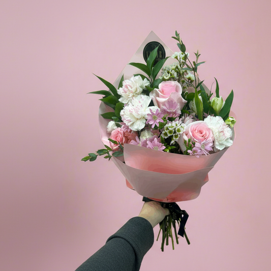Bouquet of flowers wrapped in pink paper against a pink background
