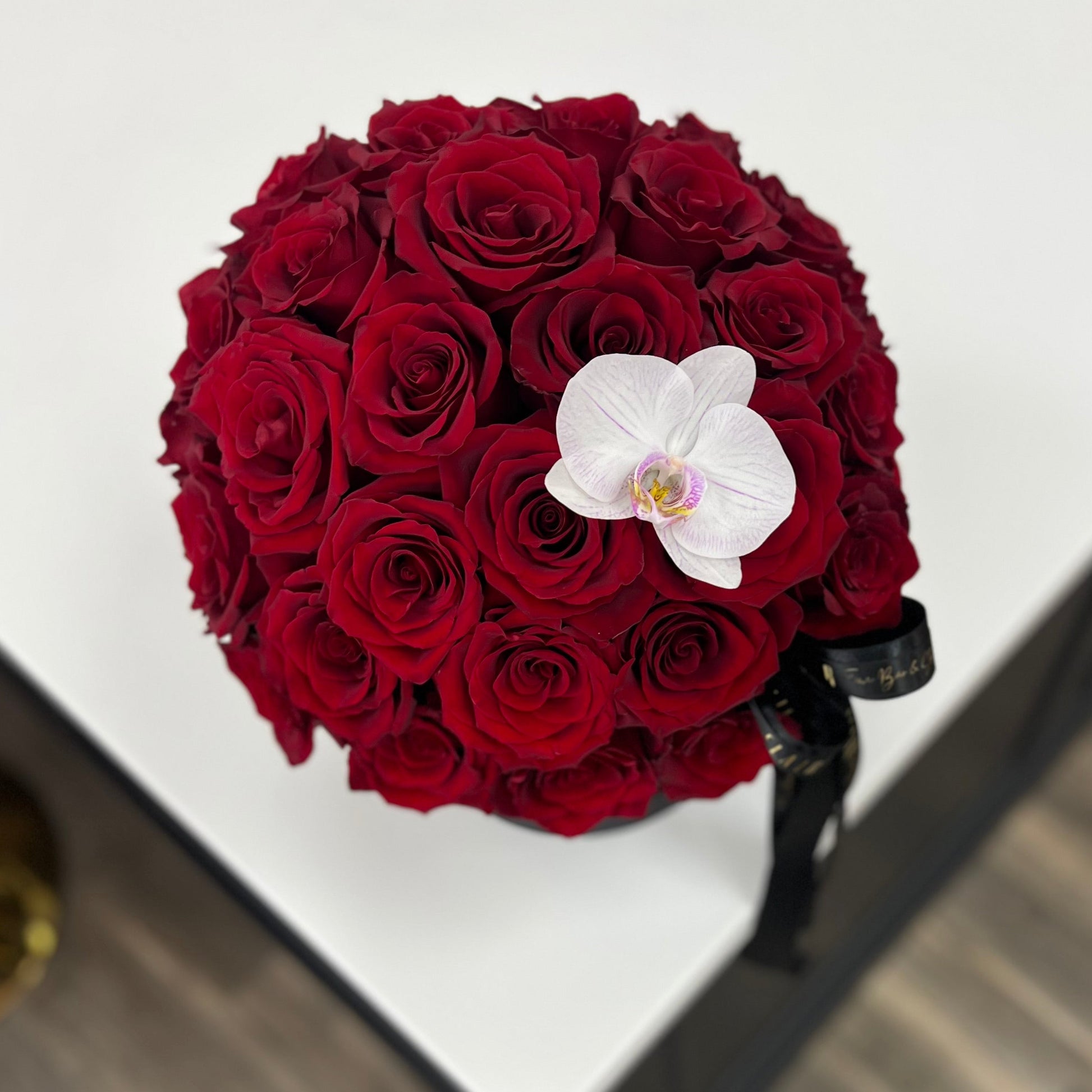 Bouquet of red roses with a white orchid on a white surface in Florence, Kentucky flower shop, Flair Flower Bar