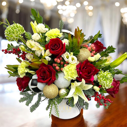 Christmas flower arrangement with red roses, greenery, and decorative ornaments in a vase.