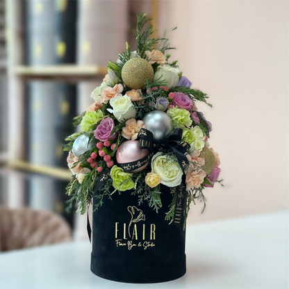 Decorative flower arrangement in a black box with 'Elair' branding on a blurred background