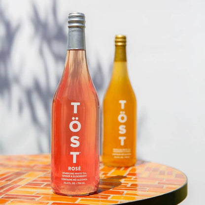 Two bottles of Töst sparkling wine on a round table with a white background