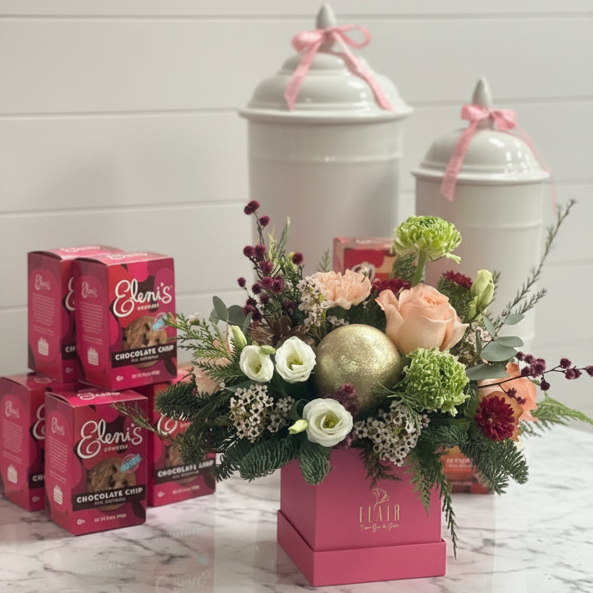 Floral Holiday arrangement in a pink box with Elani's chocolate chip cookies on a marble surface.
