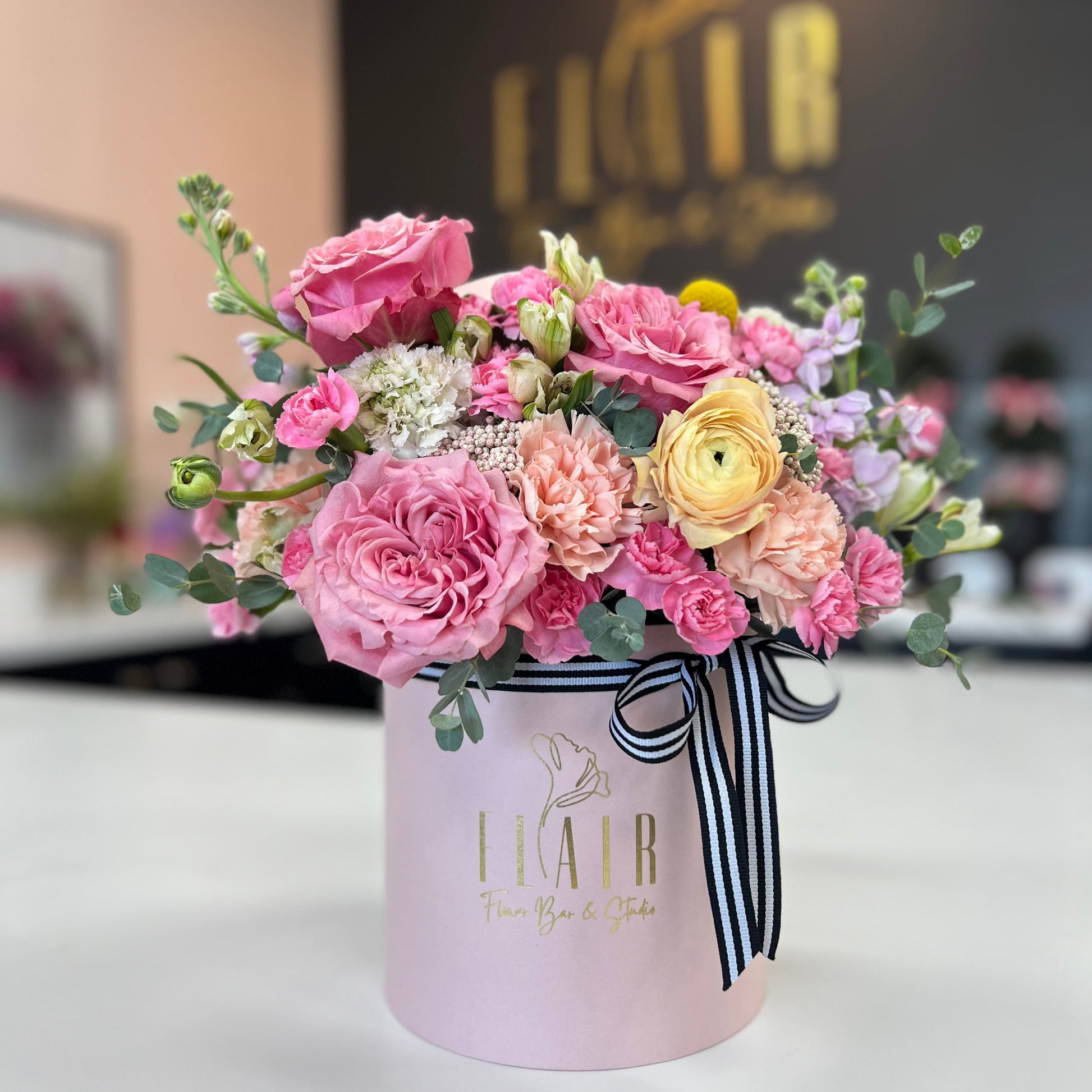 Floral arrangement in a pink box with Flair Flower Bar branding on a blurred background in Florence, Kentucky