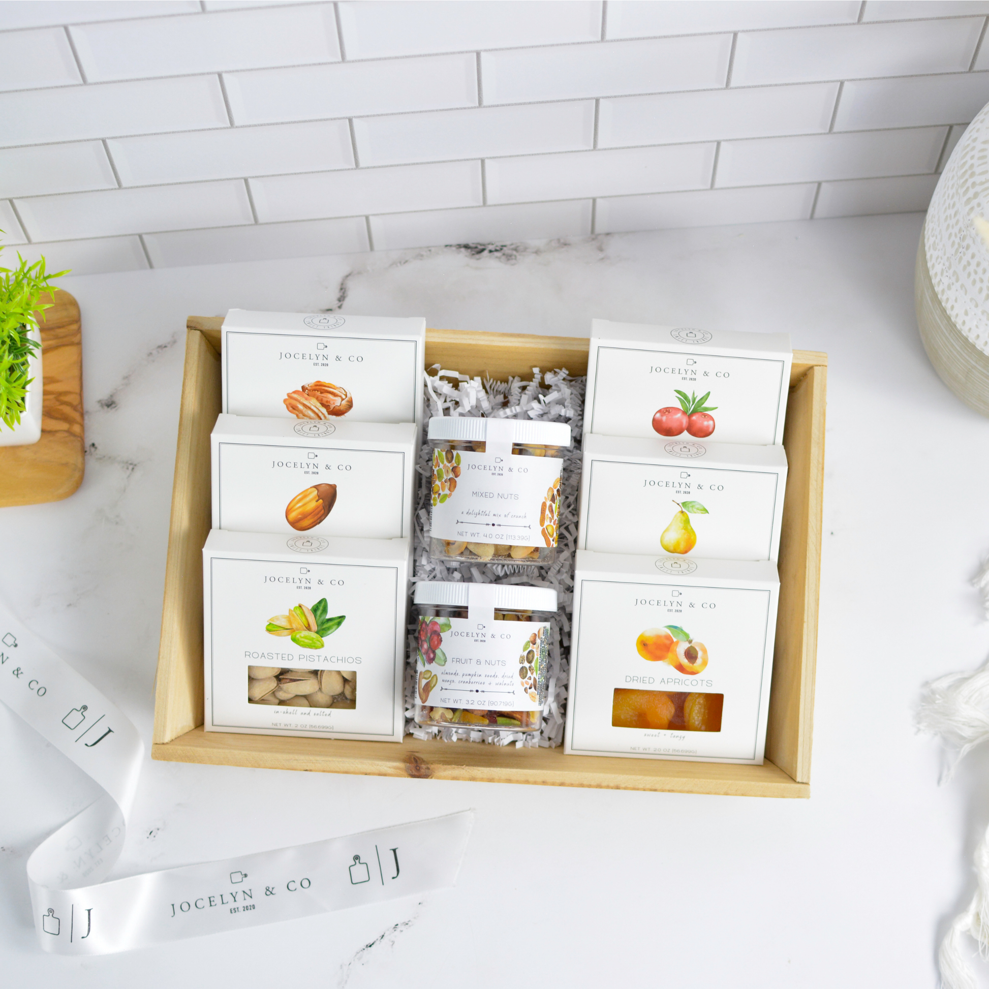 Assorted snack boxes in a wooden tray on a marble countertop with a white tiled backsplash.