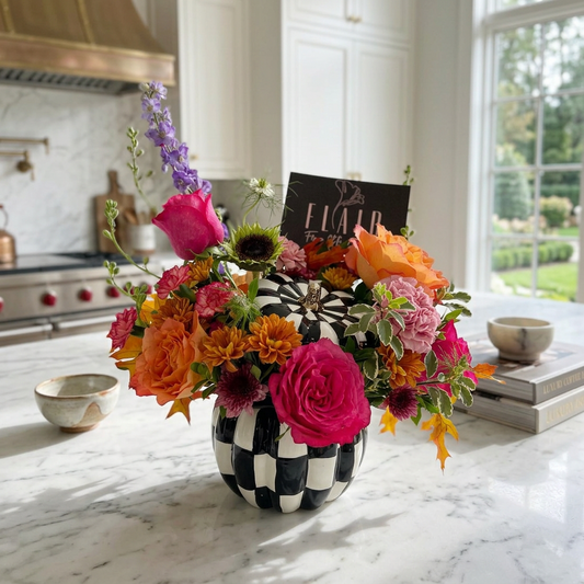 A vibrant floral arrangement in a black-and-white checkered vase on a white marble kitchen counter, perfect for gifting for Fall or Thanksgiving