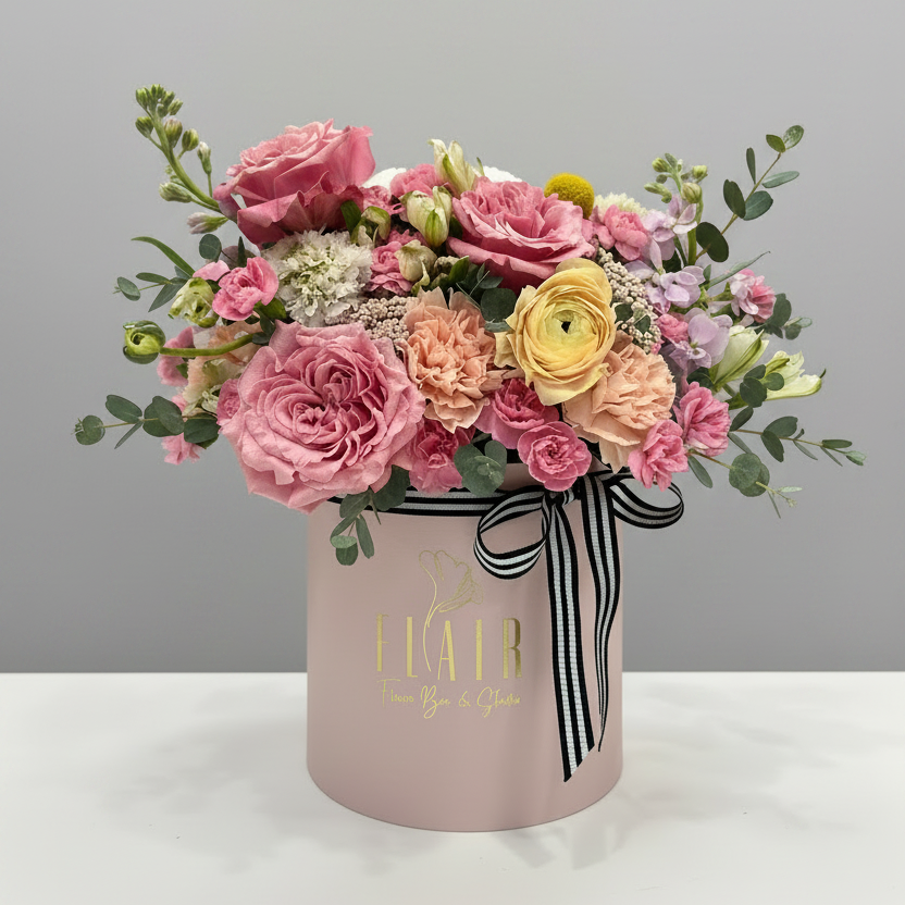Floral arrangement in a pink box with a black and white ribbon on a gray background