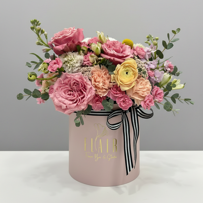 Floral arrangement in a pink box with a black and white ribbon on a gray background