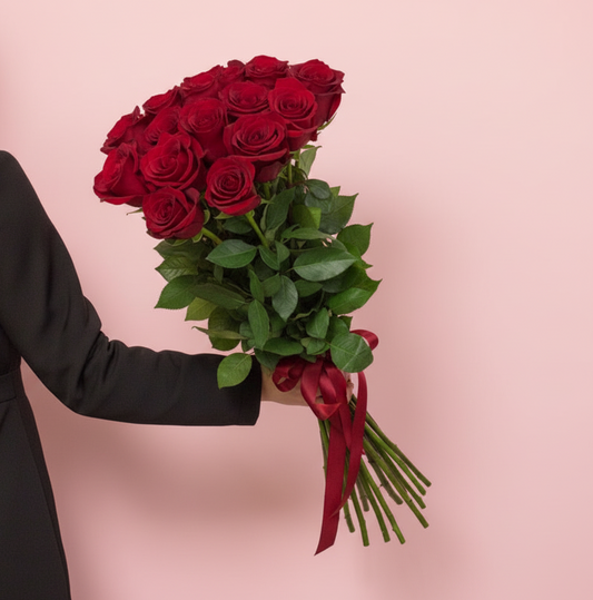 Bouquet of red roses held by a person against a pink background
