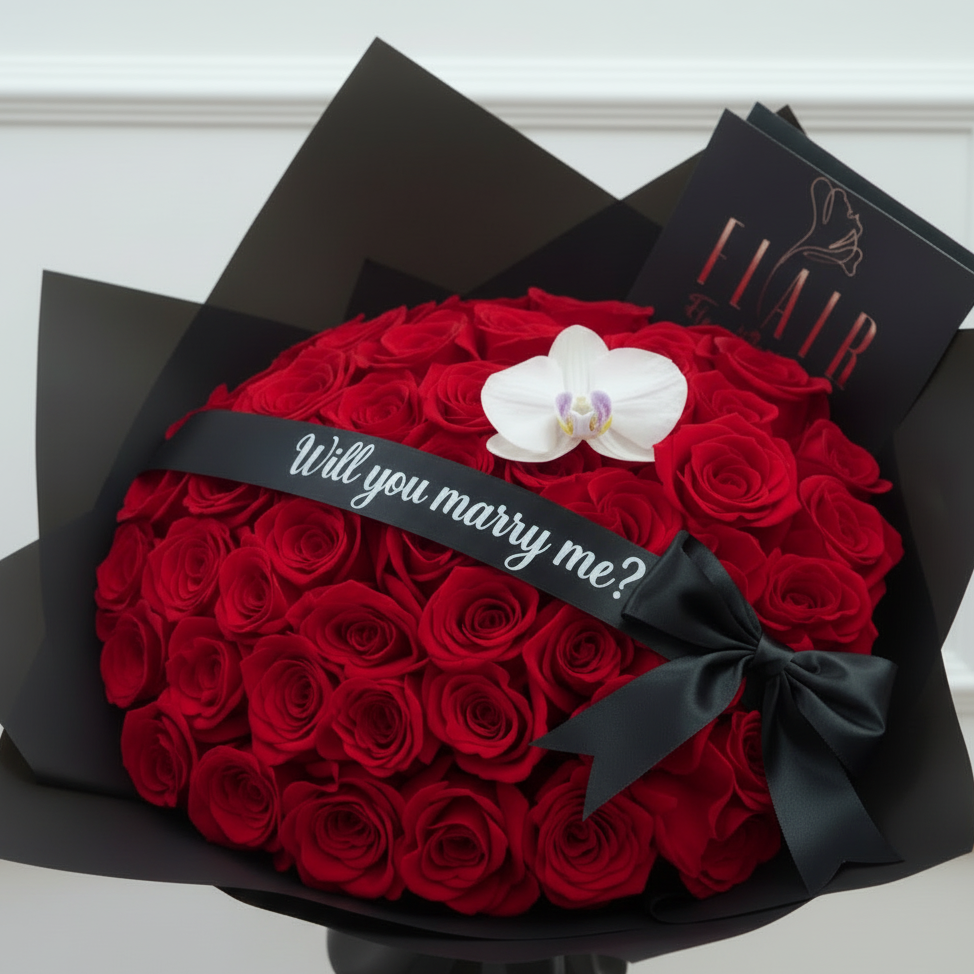 Bouquet of red roses with a white orchid and 'Will you marry me?' ribbon, wrapped in black paper.