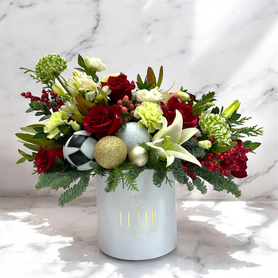 Decorative holiday flower arrangement with ornaments in a white container on a marble background