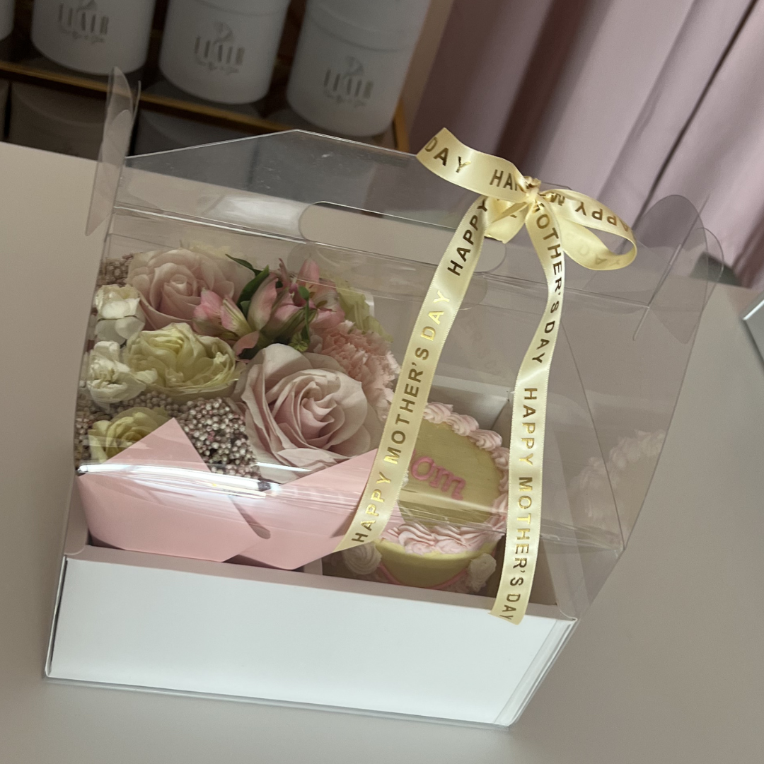 Clear box with a bouquet of flowers and a yellow ribbon on a light pink Flair boxes in background