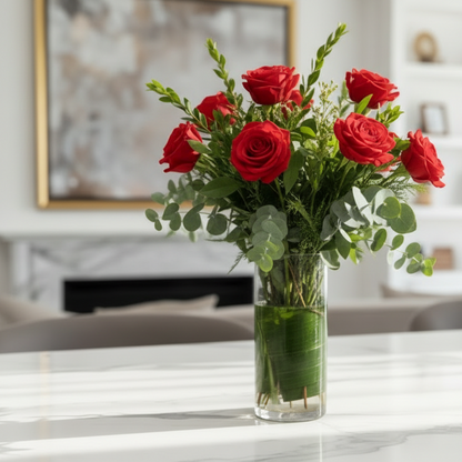 Bouquet of red roses with a decorative bow in a clear vase on a marble surface.