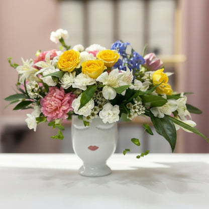 Colorful flower arrangement in a white vase on a marble surface with a blurred background